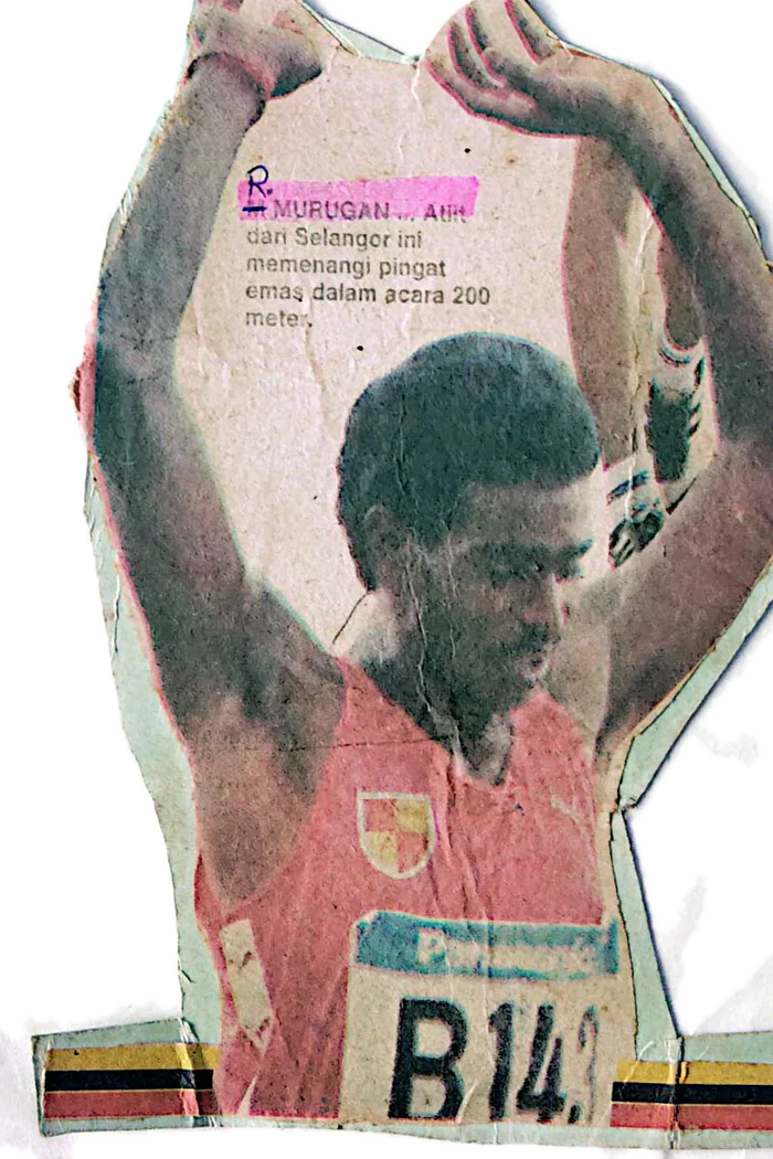 A newspaper photograph of R. Murugan with his arms raised after winning a 200m, cut out around his arms with scissors and kept in the album. A pink highlighter marks his name in the caption.