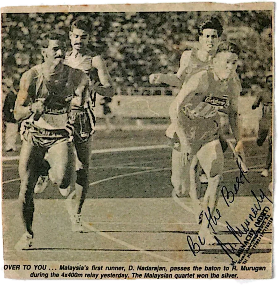 A newspaper cutting kept in the album: Malaysia's first runner hands the baton to R. Murugan in the 4×400m relay. The printed caption ends, "The Malaysian quartet won the silver." He has signed across the corner, "Be the best."
